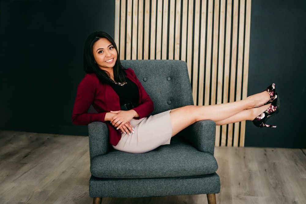 Stylish woman sitting on a gray armchair with her legs extended in a modern, professional photo.