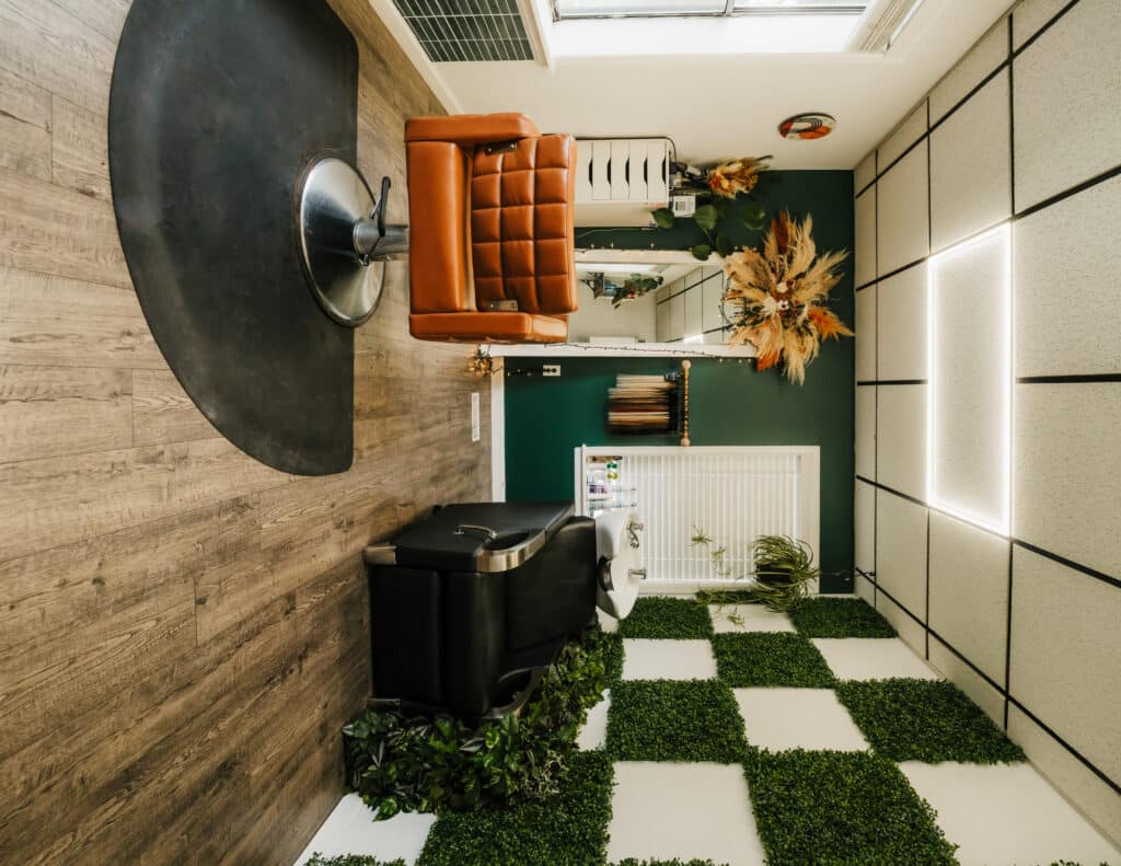 Stylish salon interior with a vintage leather chair, greenery wall decor, and hair washing station, showcasing modern and cozy hair salon design.