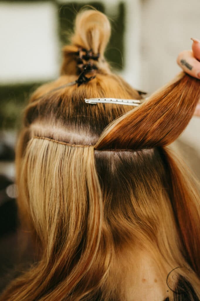 High-quality hair extensions being carefully crafted with precise sewing techniques, showcasing professional hairstyling at Cain's Candids for stunning, natural-looking blonde hair transformations.