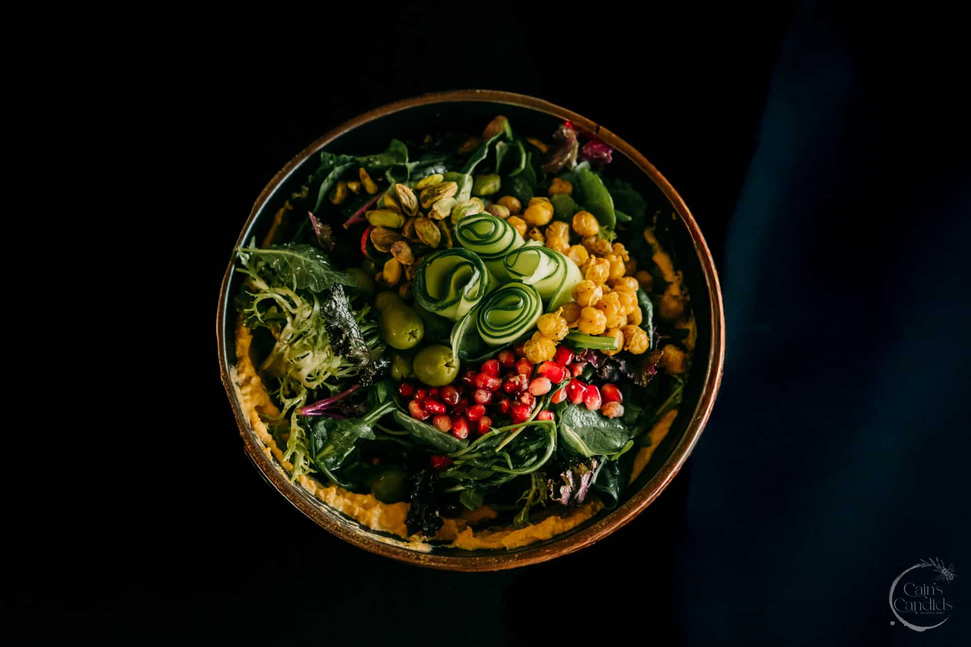 Fresh gourmet salad with mixed greens, cucumber ribbons, chickpeas, pomegranate seeds, and edible flowers in a stylish bowl, perfect for healthy eating.