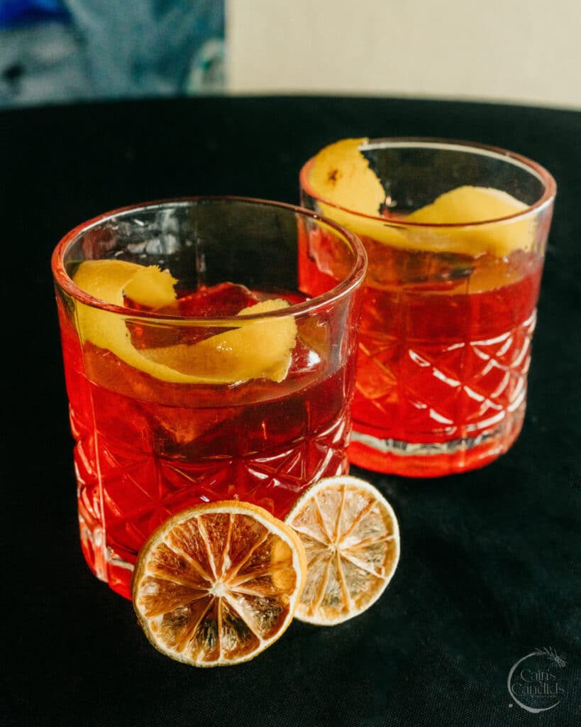 Bright red cocktails with lemon peel garnishes and dried lemon slices, served in textured glassware for a vibrant and refreshing drink presentation.